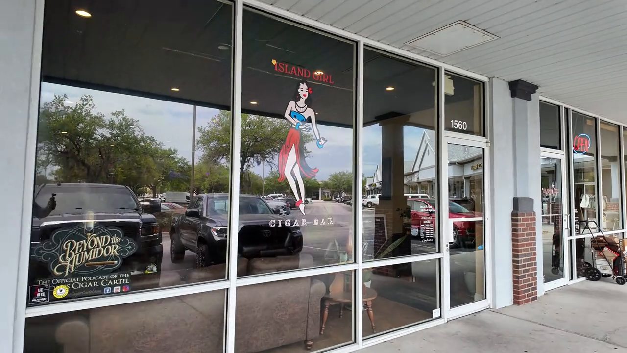 The front windows and door of Island Girl Cigar Bar, with a pin-up style illustration on the glass and the number 1560 by the door.